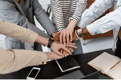 four people putting their hands in a pile in the middle of them