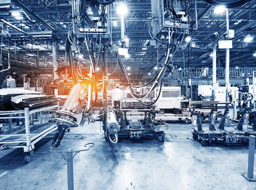 A blue toned shot of a automotive parts manufacturing factory with robotic arms highlighted by an orange glow