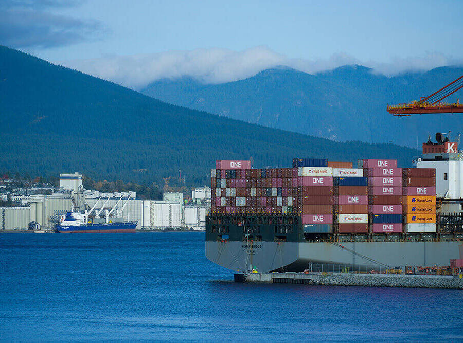 A freight ship packed high with freight pallets, on a blue, mountainous background.